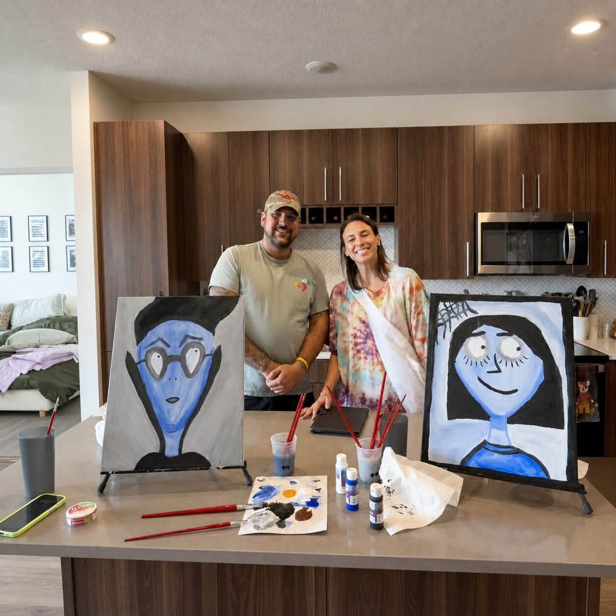 Couple with their finished Spooky Selfies date night paintings in their kitchen