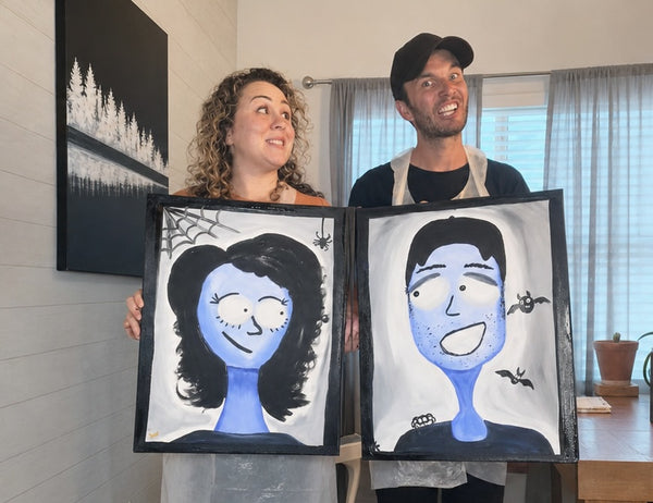 Couple holding their finished Spooky Selfies Halloween date night paintings